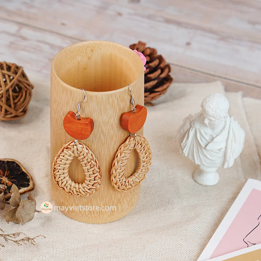 A pair of handcrafted rattan earrings with teardrop-shaped orange wooden beads, made by Mayvietstore. The earrings are made of high-quality rattan and wood, and are lightweight and comfortable to wear. The teardrop-shaped beads add a touch of elegance and sophistication to the earrings, while the rattan gives them a natural and earthy feel. The orange wooden beads add a pop of color and make the earrings stand out. These earrings are perfect for any occasion, from a casual day out to a special event.