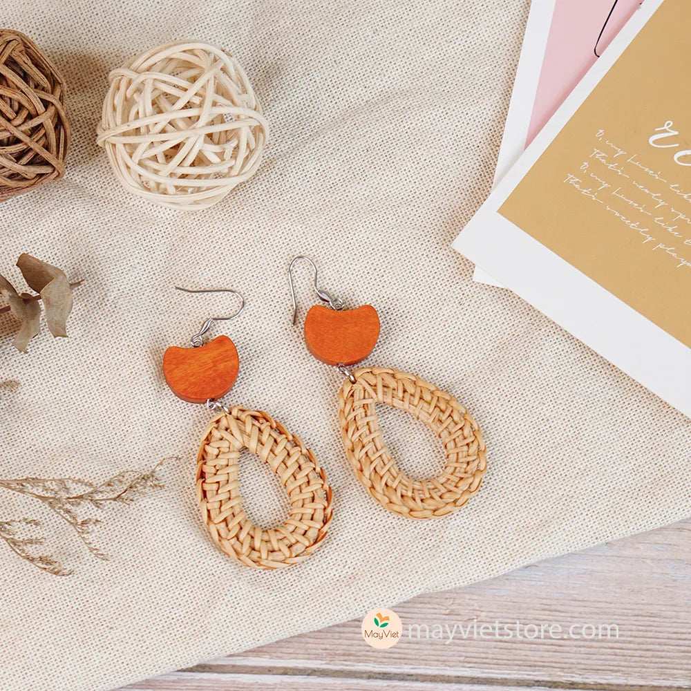 A pair of handcrafted rattan earrings with teardrop-shaped orange wooden beads, made by Mayvietstore. The earrings are made of high-quality rattan and wood, and are lightweight and comfortable to wear. The teardrop-shaped beads add a touch of elegance and sophistication to the earrings, while the rattan gives them a natural and earthy feel. The orange wooden beads add a pop of color and make the earrings stand out. These earrings are perfect for any occasion, from a casual day out to a special event.