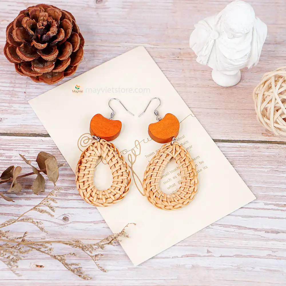 A pair of handcrafted rattan earrings with teardrop-shaped orange wooden beads, made by Mayvietstore. The earrings are made of high-quality rattan and wood, and are lightweight and comfortable to wear. The teardrop-shaped beads add a touch of elegance and sophistication to the earrings, while the rattan gives them a natural and earthy feel. The orange wooden beads add a pop of color and make the earrings stand out. These earrings are perfect for any occasion, from a casual day out to a special event.