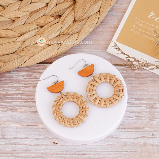 A pair of handcrafted rattan hoop earrings with orange wooden beads, made by Mayvietstore. The earrings are made of high-quality rattan and wood, and are lightweight and comfortable to wear. The rattan hoops are a classic style that is perfect for everyday wear, while the orange wooden beads add a touch of color and personality. These earrings are perfect for any occasion, from a casual day out to a special event.