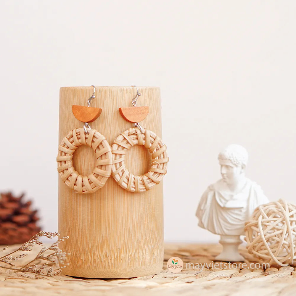 A pair of handcrafted rattan hoop earrings with orange wooden beads, made by Mayvietstore. The earrings are made of high-quality rattan and wood, and are lightweight and comfortable to wear. The rattan hoops are a classic style that is perfect for everyday wear, while the orange wooden beads add a touch of color and personality. These earrings are perfect for any occasion, from a casual day out to a special event.
