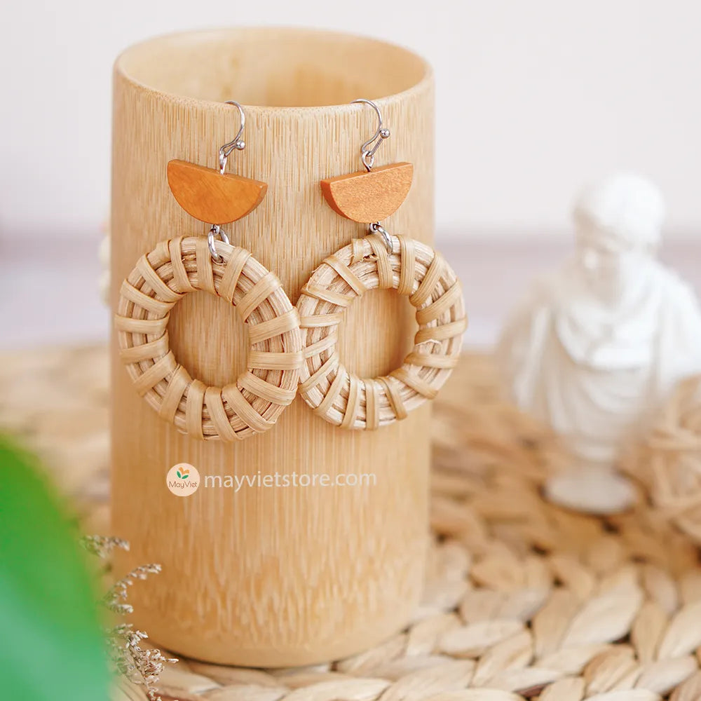A pair of handcrafted rattan hoop earrings with orange wooden beads, made by Mayvietstore. The earrings are made of high-quality rattan and wood, and are lightweight and comfortable to wear. The rattan hoops are a classic style that is perfect for everyday wear, while the orange wooden beads add a touch of color and personality. These earrings are perfect for any occasion, from a casual day out to a special event.
