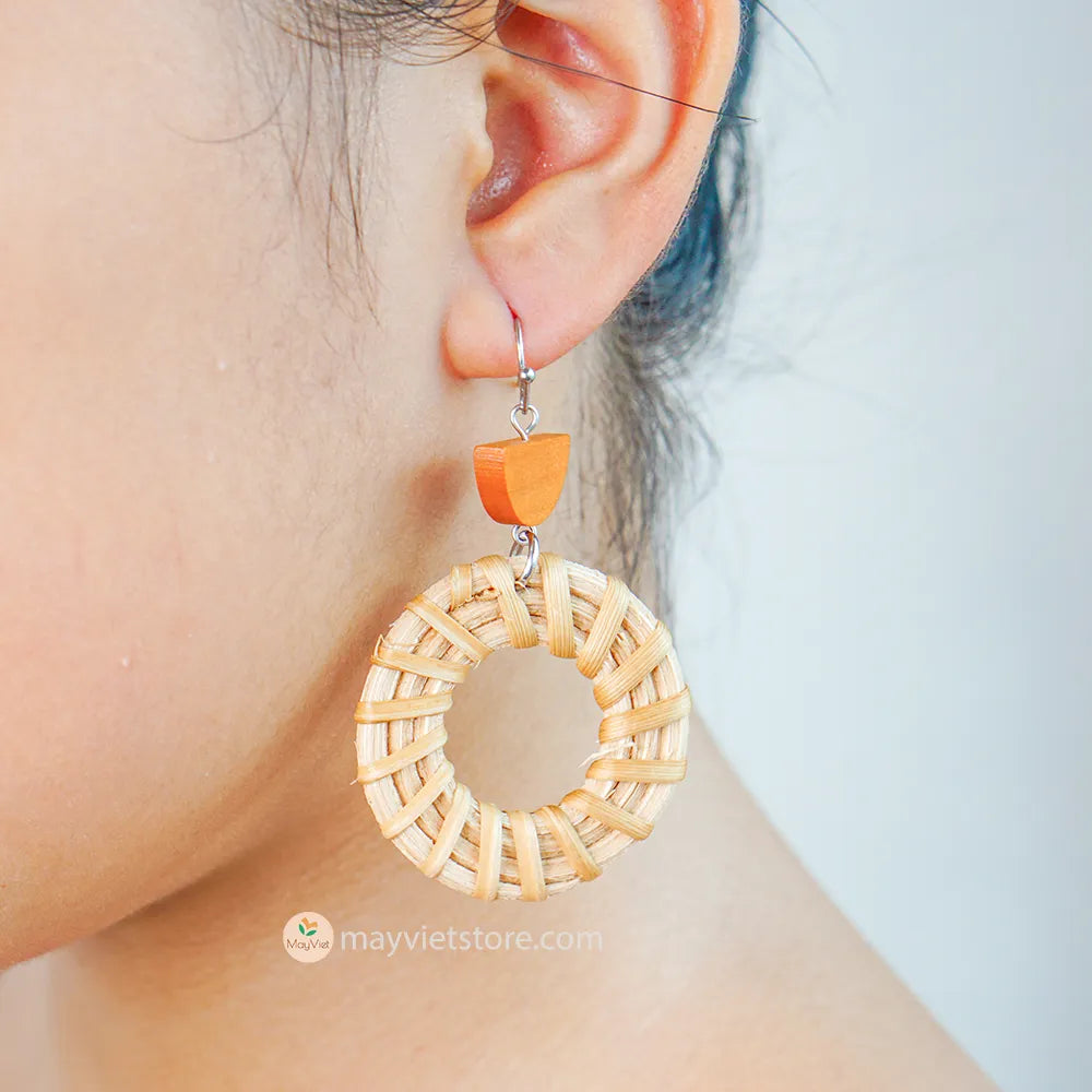 A pair of handcrafted rattan hoop earrings with orange wooden beads, made by Mayvietstore. The earrings are made of high-quality rattan and wood, and are lightweight and comfortable to wear. The rattan hoops are a classic style that is perfect for everyday wear, while the orange wooden beads add a touch of color and personality. These earrings are perfect for any occasion, from a casual day out to a special event.